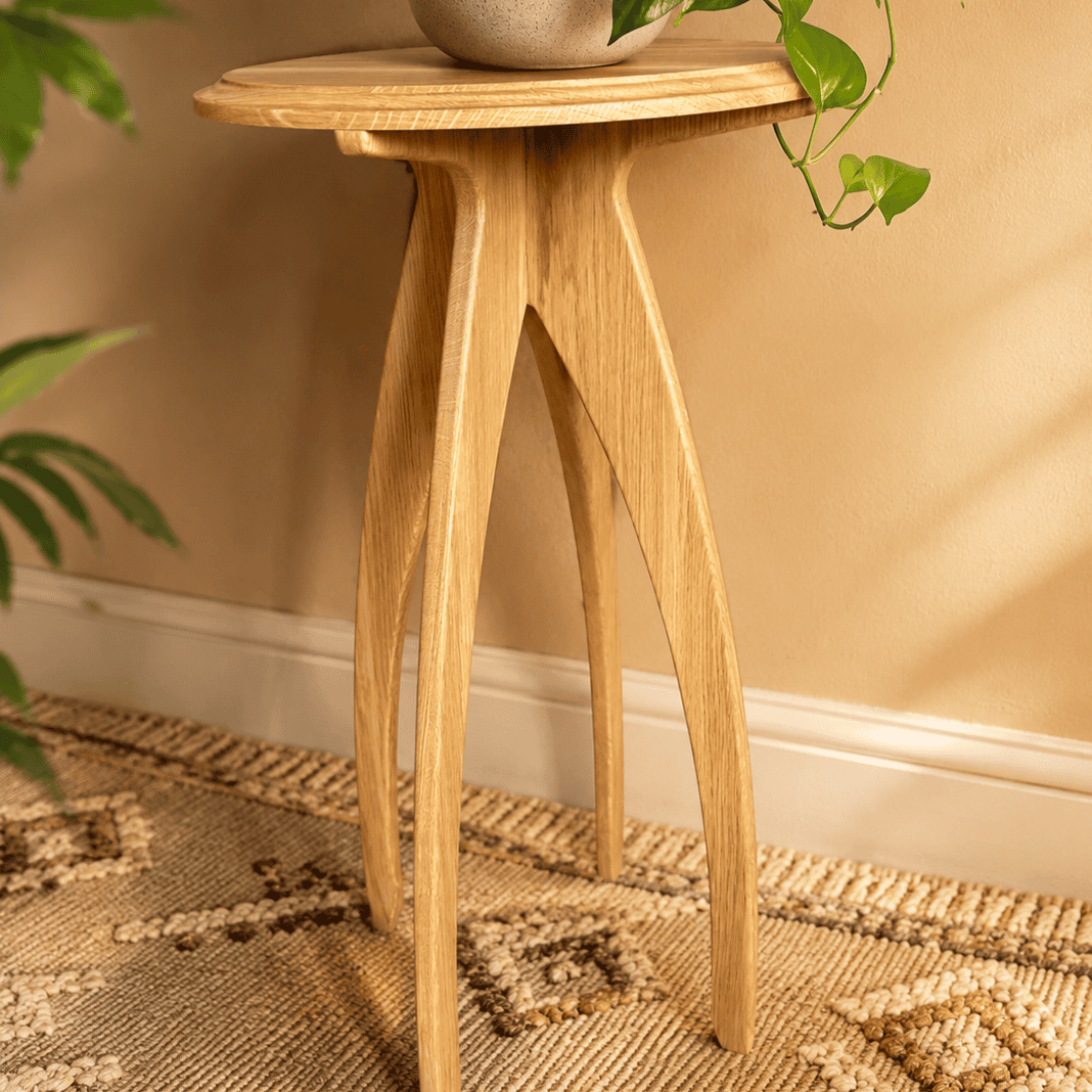 Handcrafted solid wood plant stand with sculptural curved legs and round top in a warm modern interior.